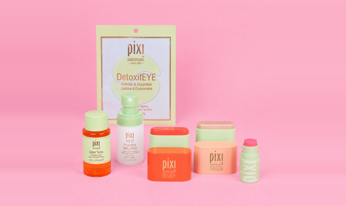 Pixi skincare set arranged on a pink background, including a DetoxiEYE pouch, cleansing wipes, blush, superglow, toner, serum, and a lip treatment. The products feature pastel and bright colors like orange, coral, mint green, and peach.