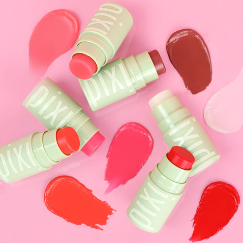 Four Pixi +HydraLip Treat sticks in pale Pixi green packaging arranged on a pink background with corresponding swatches in pink, coral, brown and red. view 2