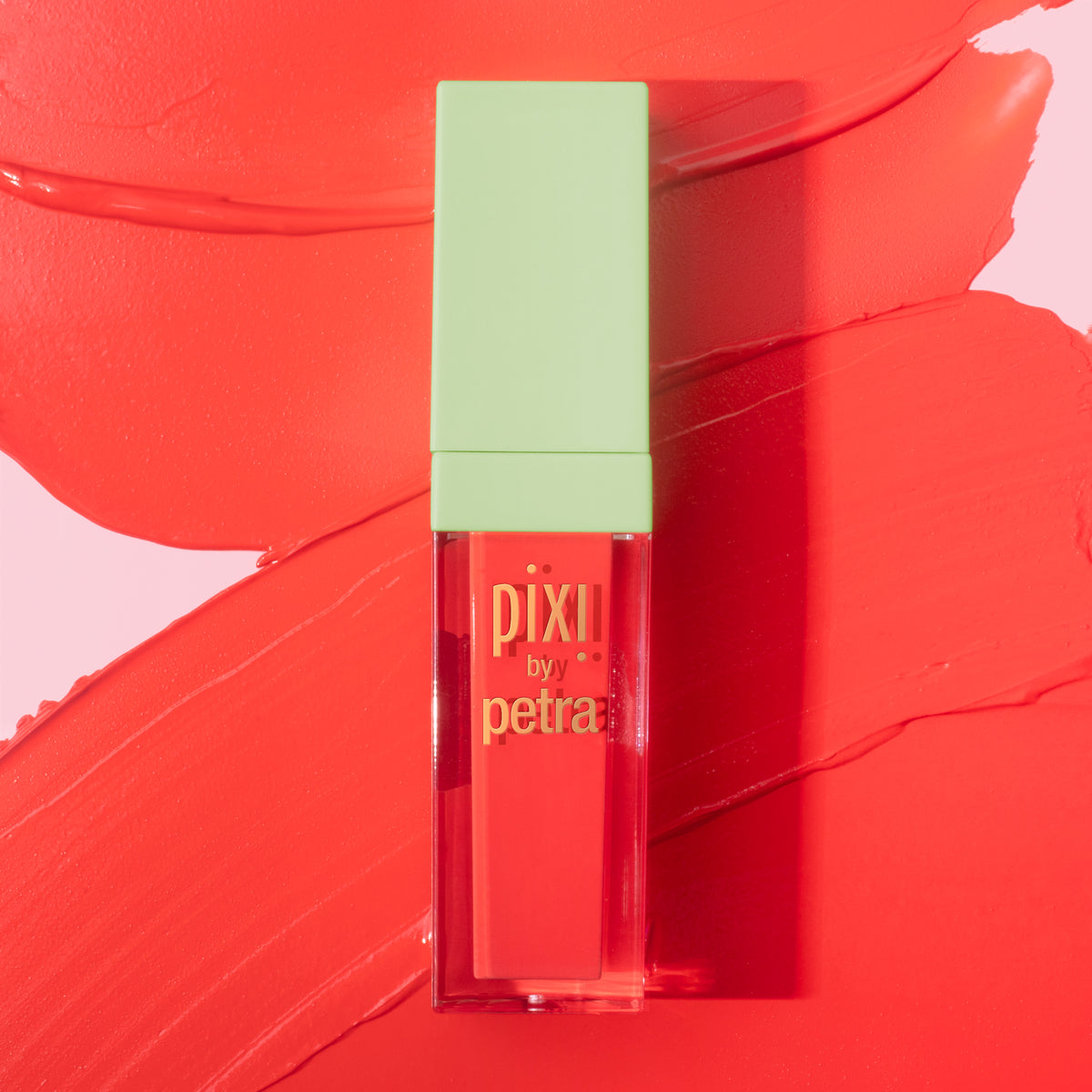 Pixii by Petra liquid lipstick in a clear rectangular tube with a light green cap, set against a vibrant coral-red background with a matching lipstick smear.