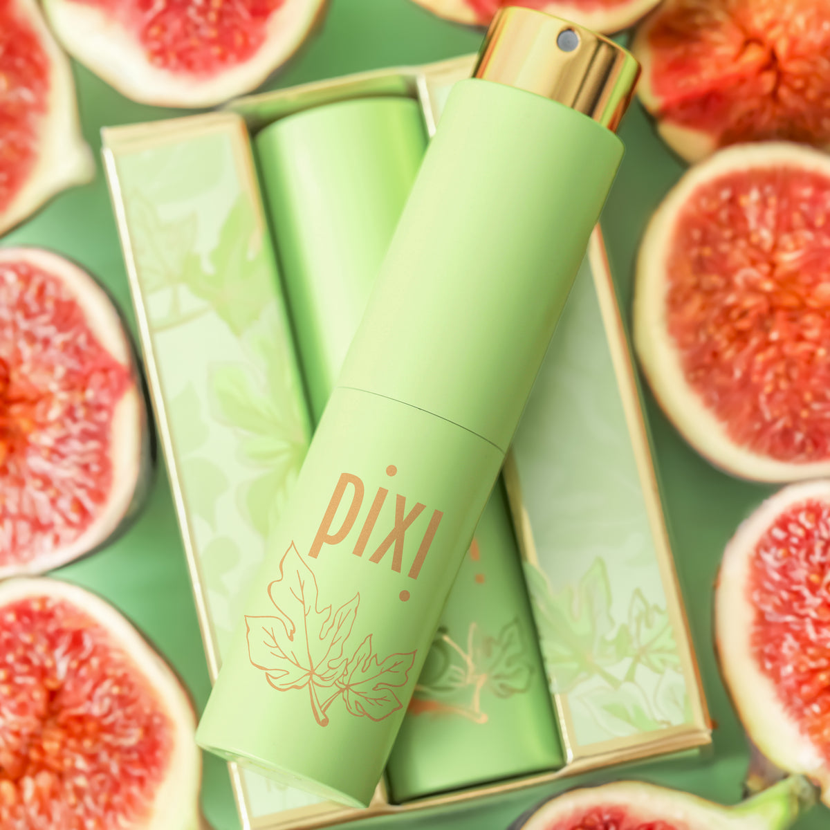 A Pixi Perfume spray bottle in light green with a gold cap, displayed diagonally on top of its matching green box, surrounded by sliced pink figs on a green background.